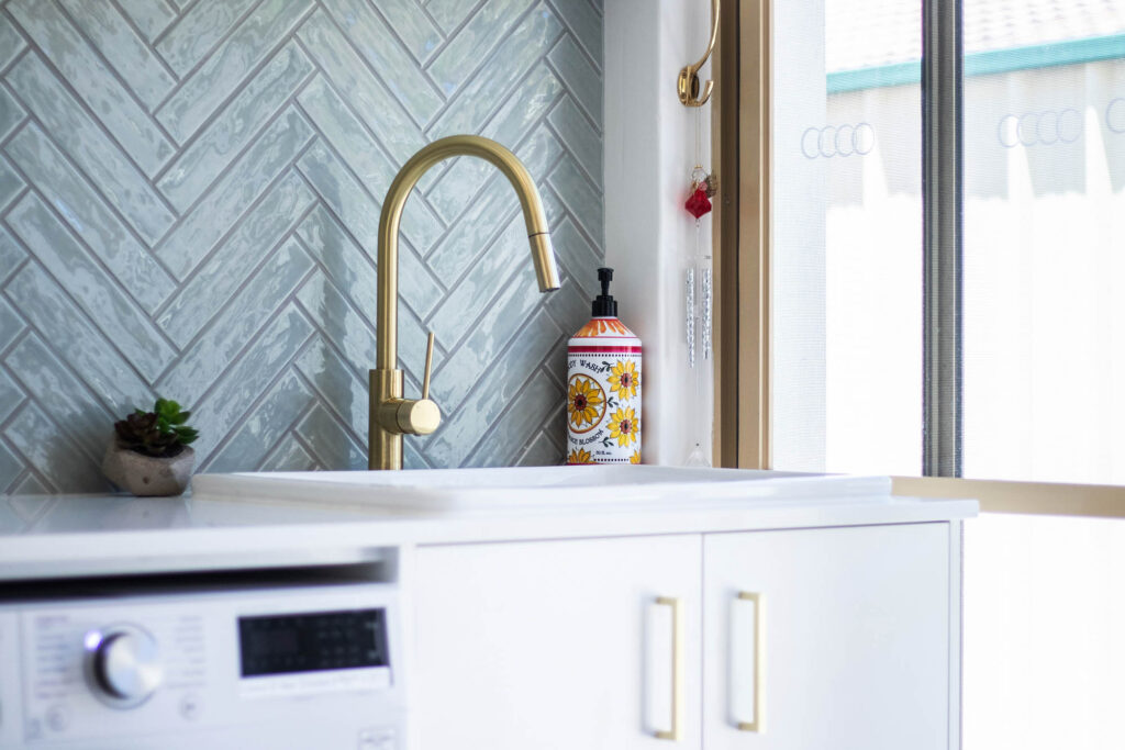 Laundry designs with beautiful fishbone tiles, brass fixings, and white cabinetry