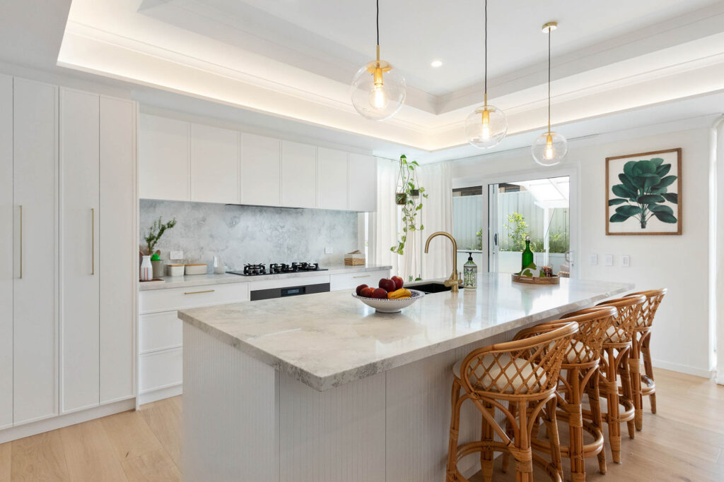 A beautiful coffered ceiling over a modern white kitchen boasting an island and stone bench tops.