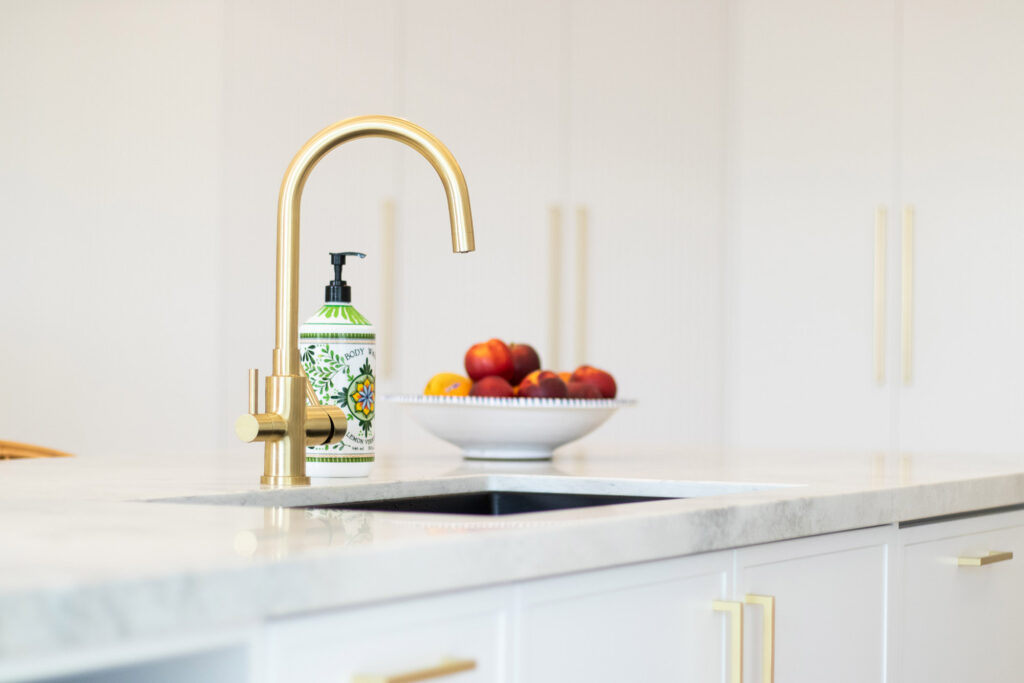 Kitchen details, showcasing brass fixings on white cabinetry and a large kitchen island with a stone bench top.