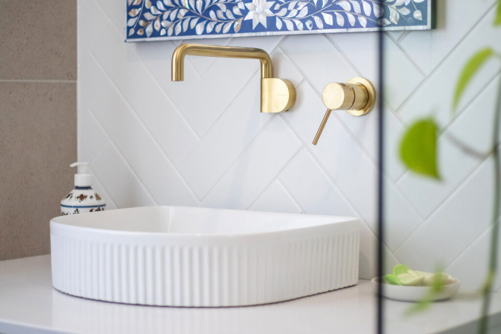 Brass fixings on white tiles and a round porcelain basin in a new built Perth bathroom.