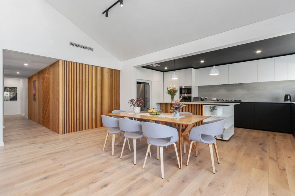 Timber clad walls, leading from the hallway into the open plan kitchen and dining area, boasting black and white cabinetry and a stone splash back.