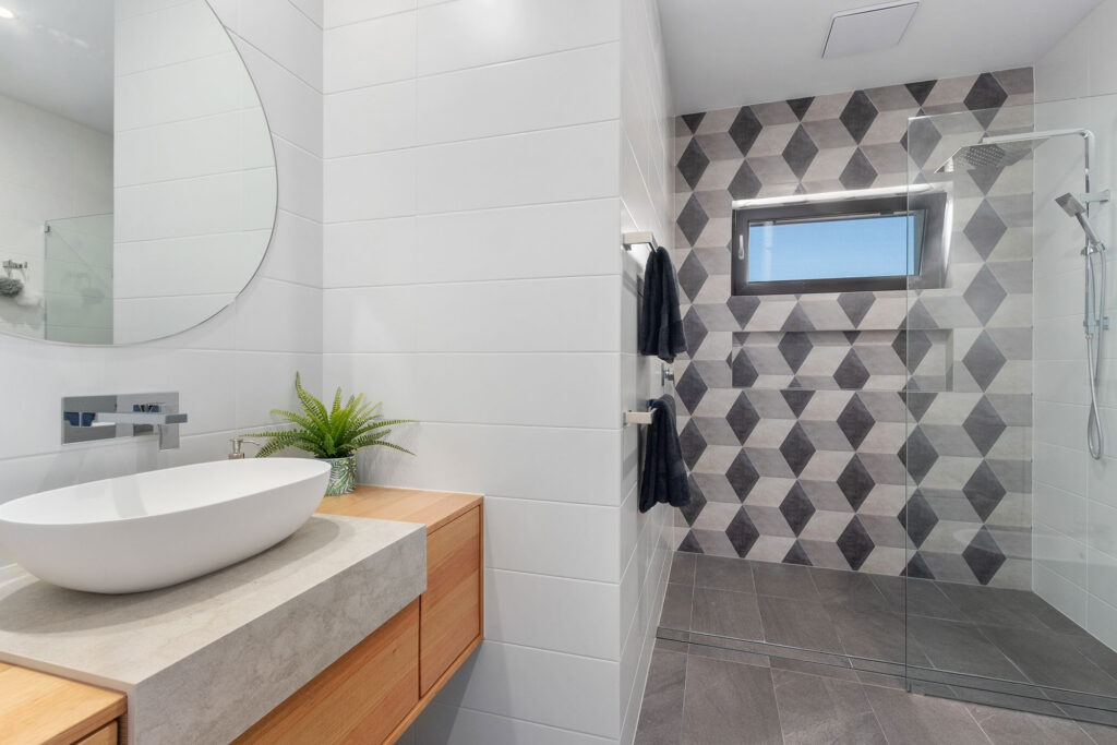 A large bathroom with a optical illusion tiled feature wall, a walk in shower and timber vanity with a round basin.
